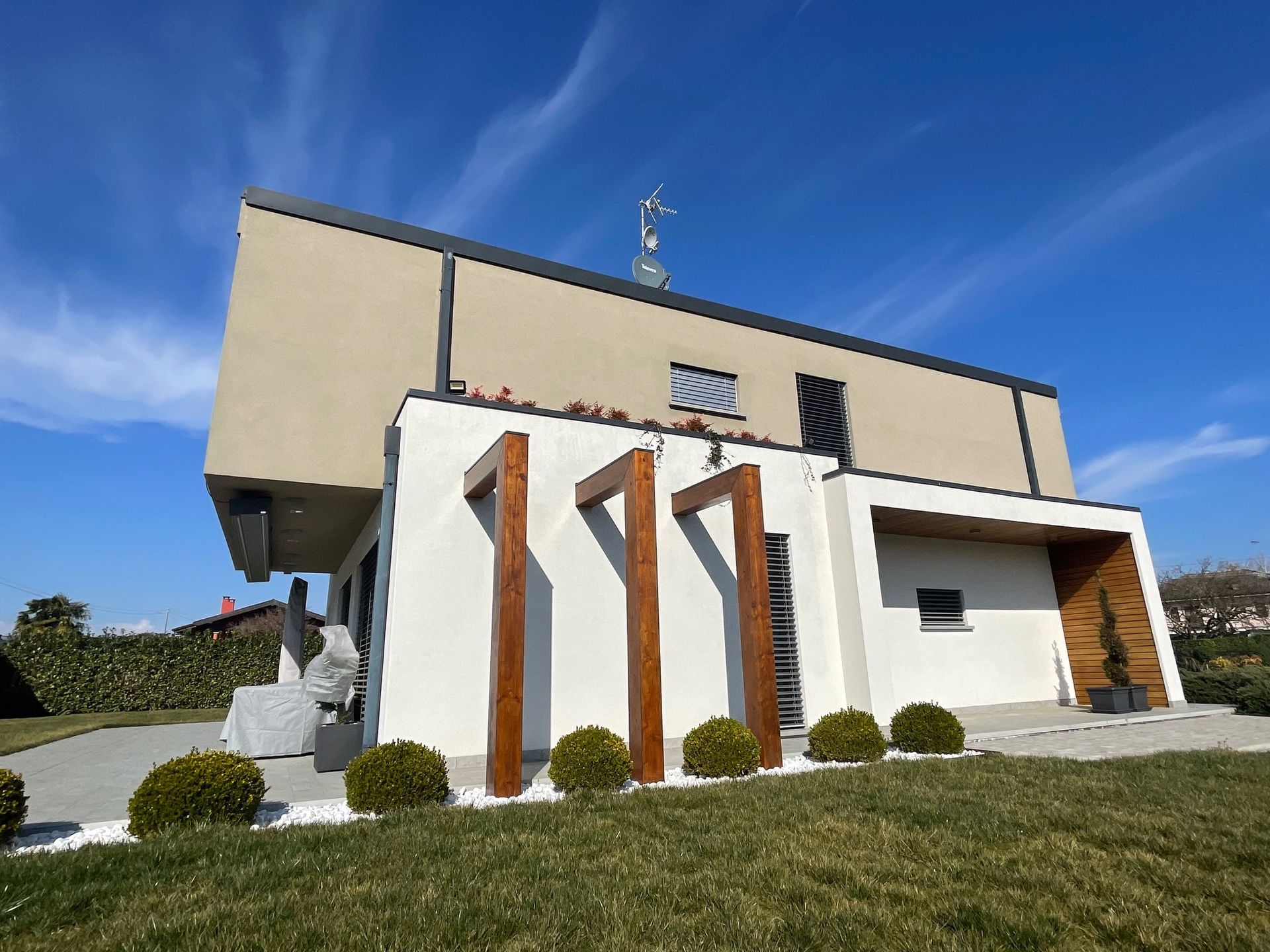 Casa moderna bianca dal design angolare, con dettagli in legno e cielo azzurro sopra un prato erboso.