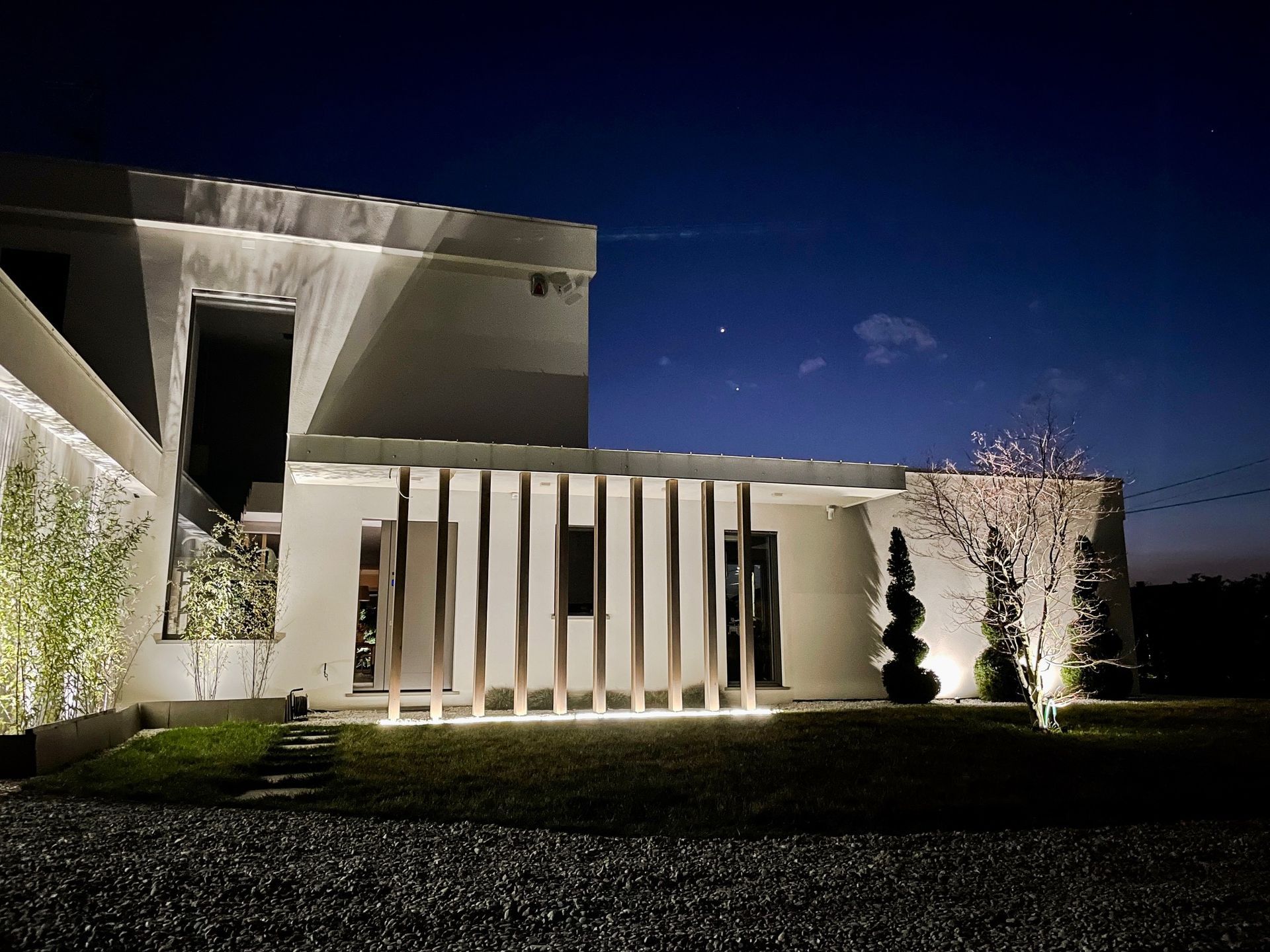 Casa moderna bianca illuminata di notte da lamelle verticali e un cielo blu scuro