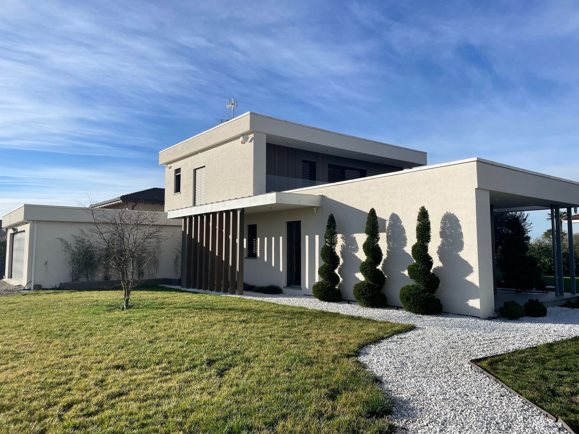 Casa moderna bianca con un sentiero curvo in pietra, prato verde e cielo azzurro.
