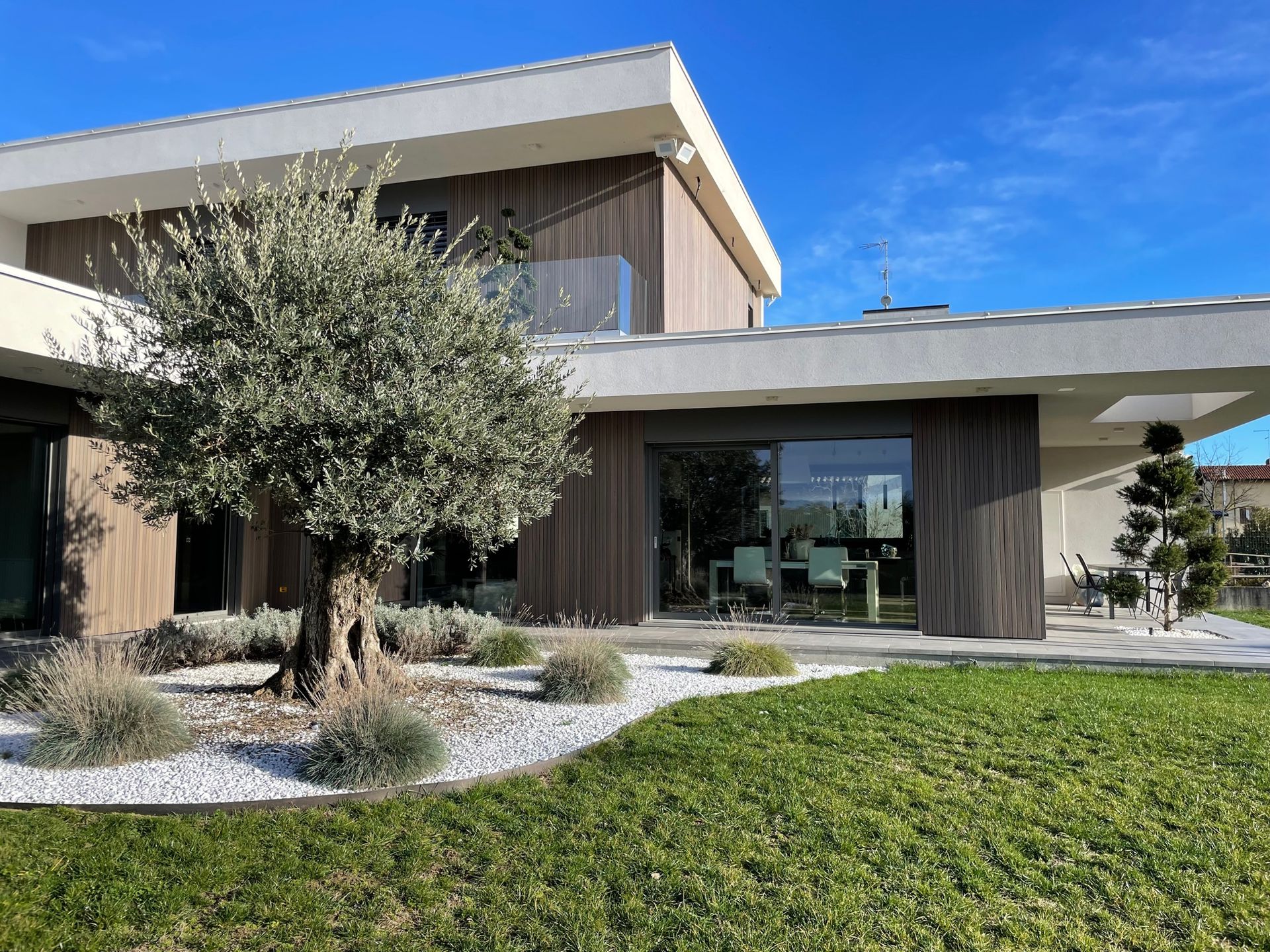 Esterno di una casa moderna con un albero, un giardino curato e un cielo azzurro limpido.
