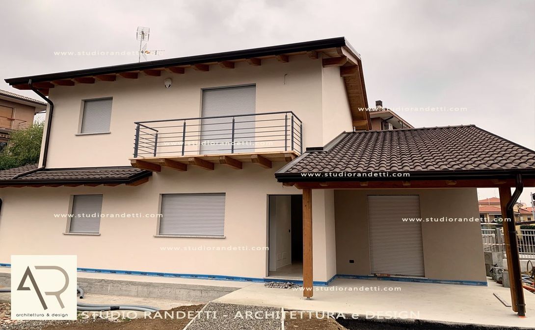 Casa a due piani beige con tetto marrone, balcone e posto auto coperto annesso, situata in una zona residenziale.