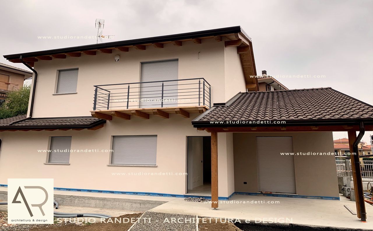 Casa a due piani beige con tetto marrone, balcone e posto auto coperto annesso, situata in una zona residenziale.