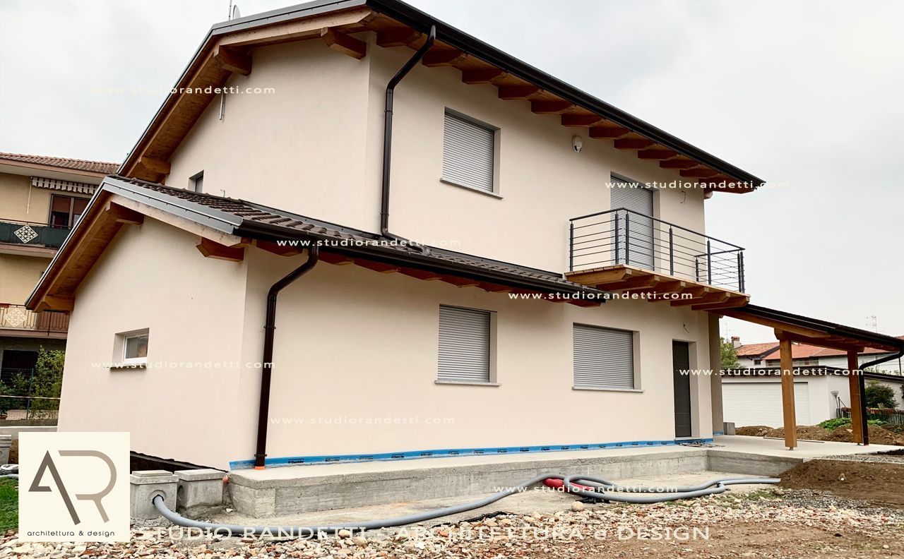 Casa beige a due piani con tetto marrone e piccolo balcone su un lotto di ghiaia