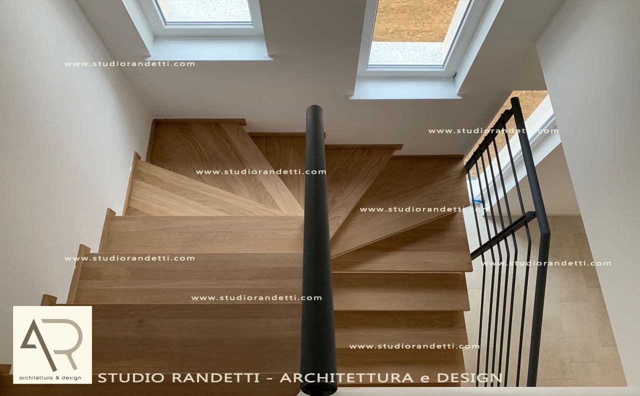 Scala moderna in legno con corrimano centrale nero e lucernari sovrastanti, vista dal pianerottolo.