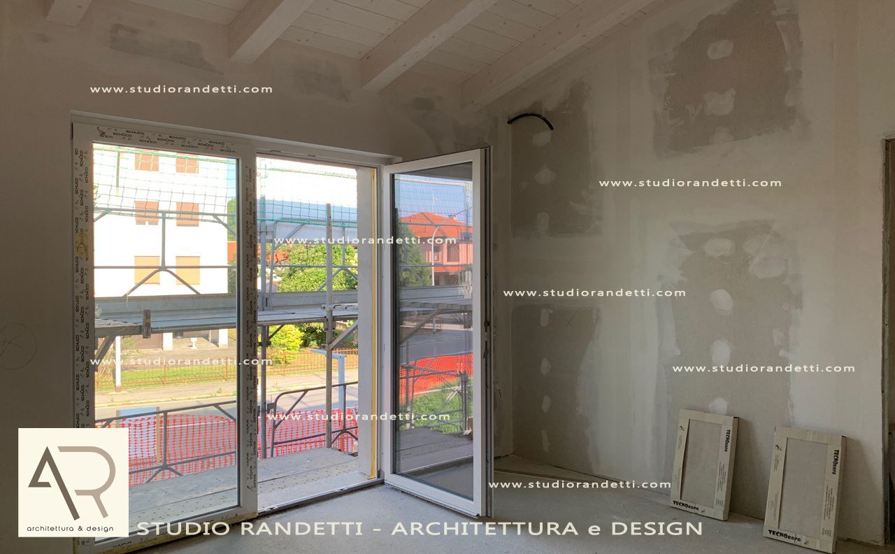 Camera ristrutturata con ampia finestra e porte a vetri, pareti bianche, travi a vista e vista sulla città.