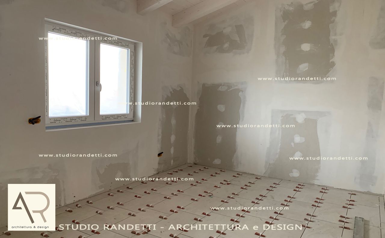 Stanza in gesso non rifinita con due finestre, pareti bianche e pavimento protettivo durante i lavori di ristrutturazione.