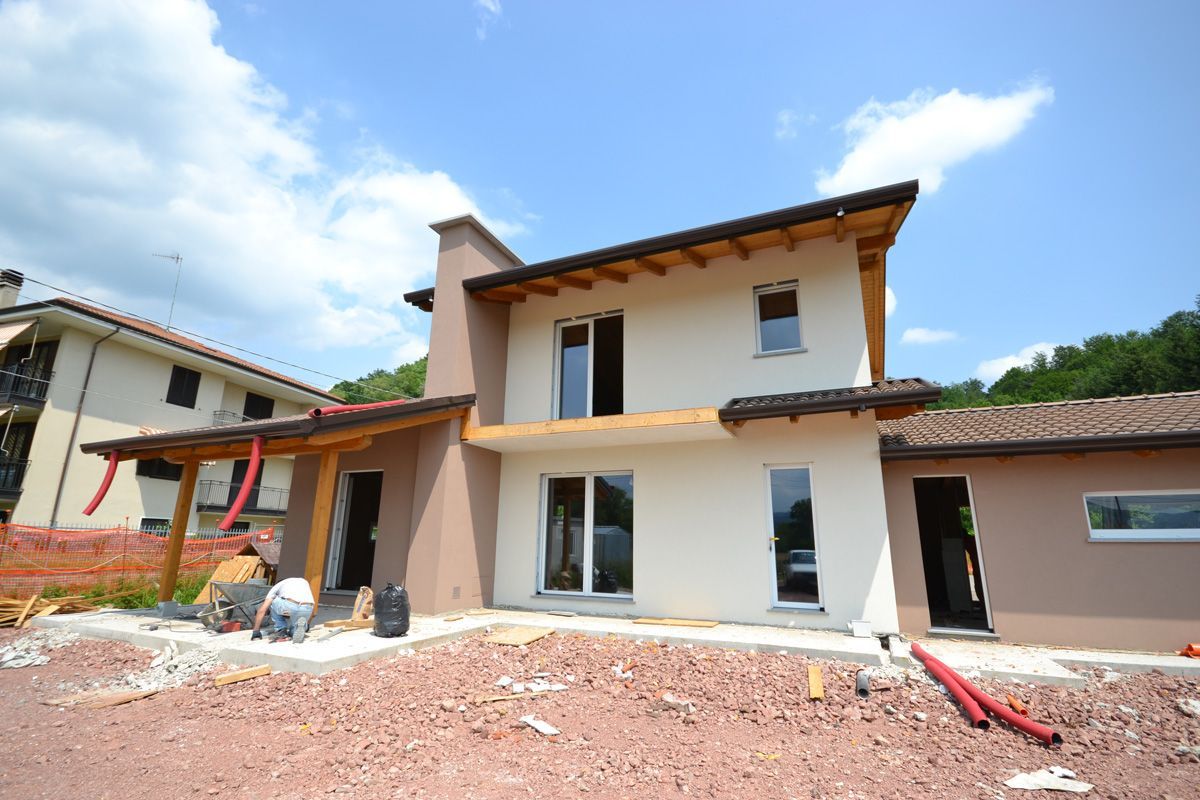 Casa a due piani in costruzione con pareti bianche, finiture marroni e terra rossa in primo piano.
