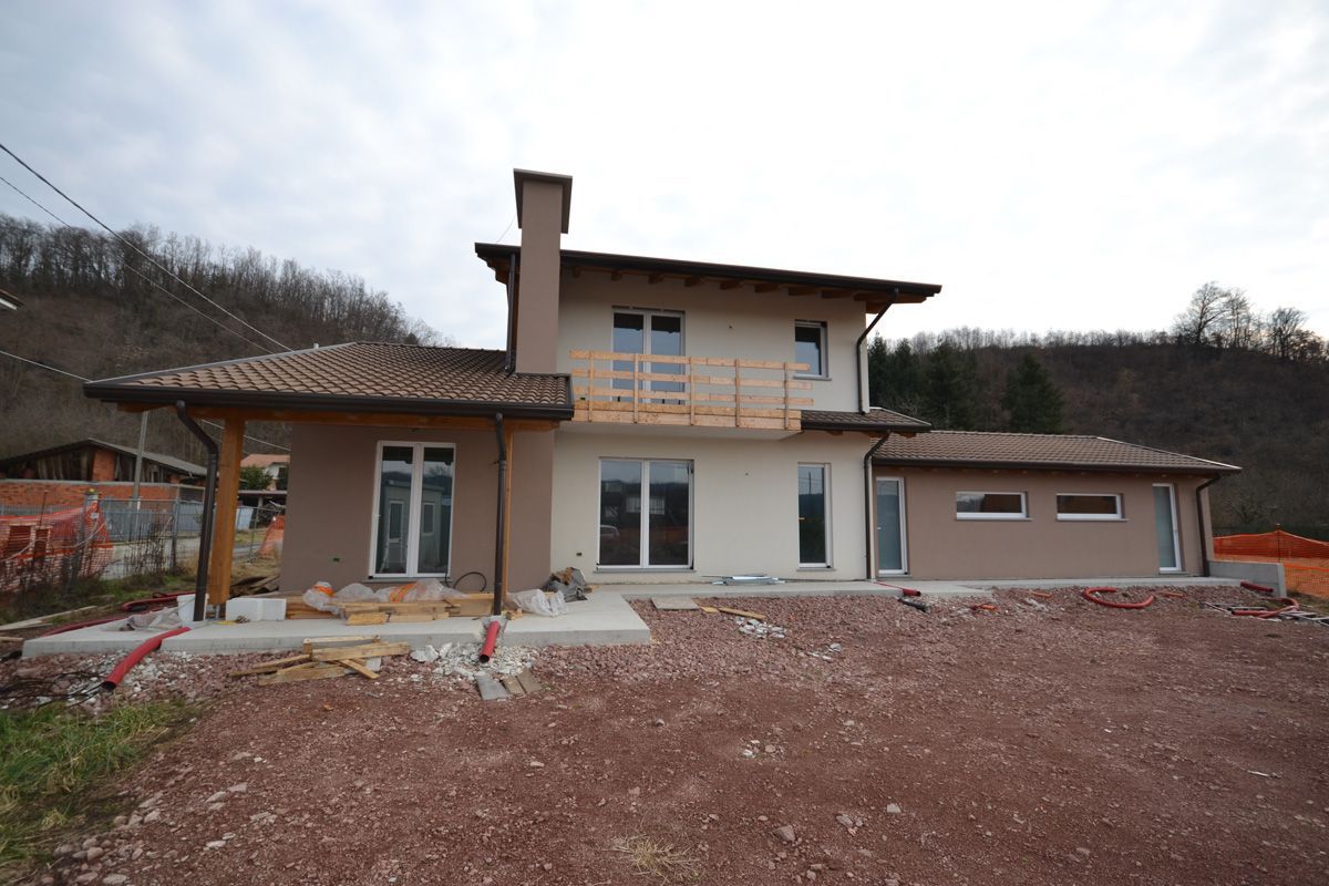 Nuova casa beige con tetto in tegole e ampie finestre su un lotto di terreno edificabile.