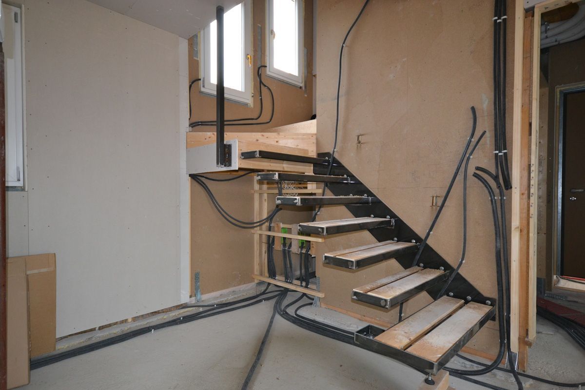 Vano scale in costruzione, ancora in fase di completamento, con cavi elettrici a vista e gradini in metallo in un interno beige.