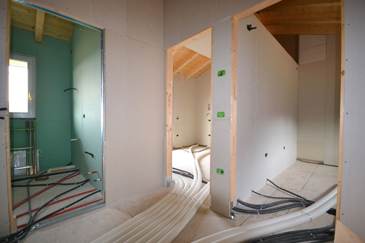 Interni non rifiniti con porte aperte, cavi elettrici a vista e pavimenti coperti in una casa in fase di ristrutturazione.