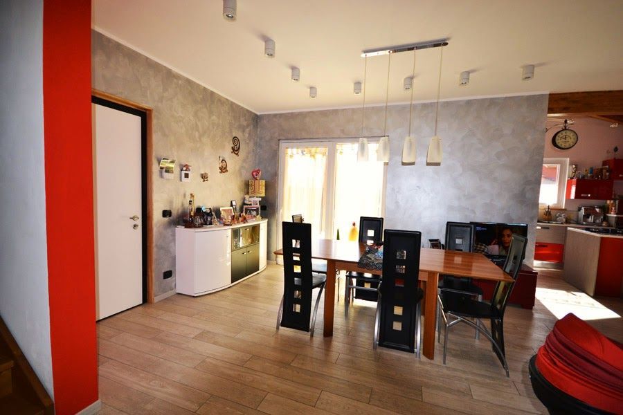 Sala da pranzo moderna con tavolo in legno, sedie nere, angolo cottura e parete decorativa rossa.