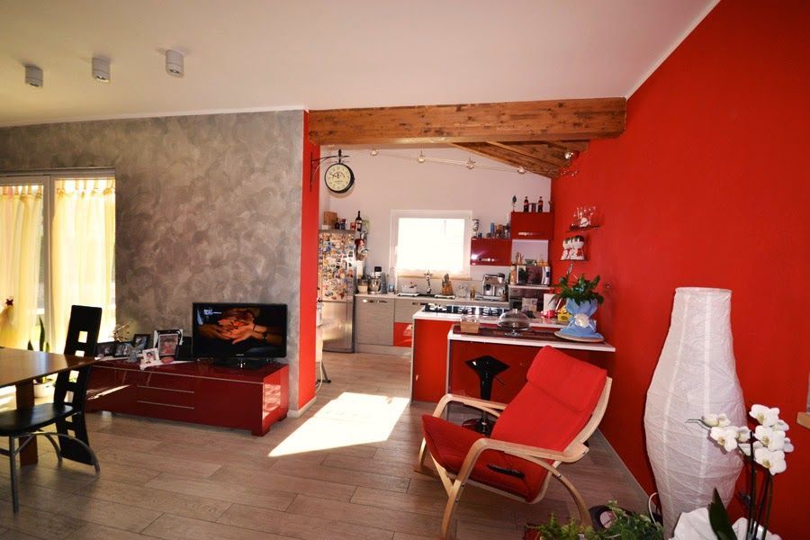 Soggiorno moderno con parete d'accento rossa, poltrona bianca e vista aperta sulla cucina.