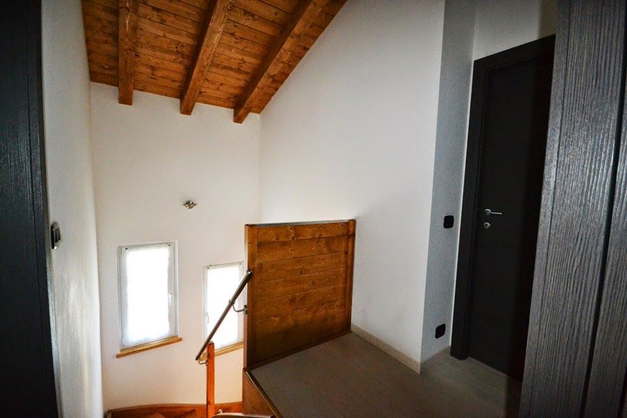 Pianerottolo interno delle scale con pareti bianche, travi in ​​legno a vista e una porta scura.