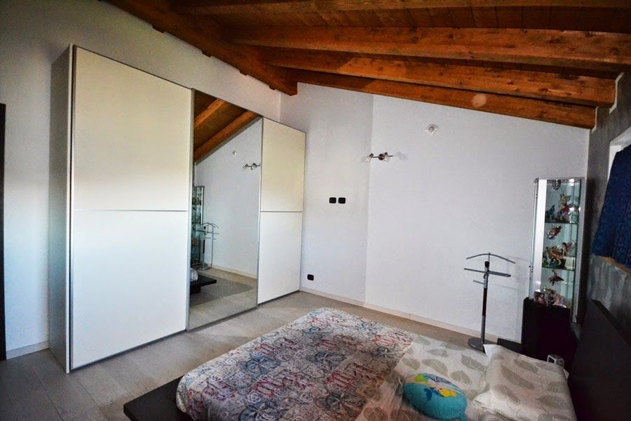 Mansarda vuota con soffitto in legno inclinato, pareti bianche, armadio e tappeto a motivi geometrici.