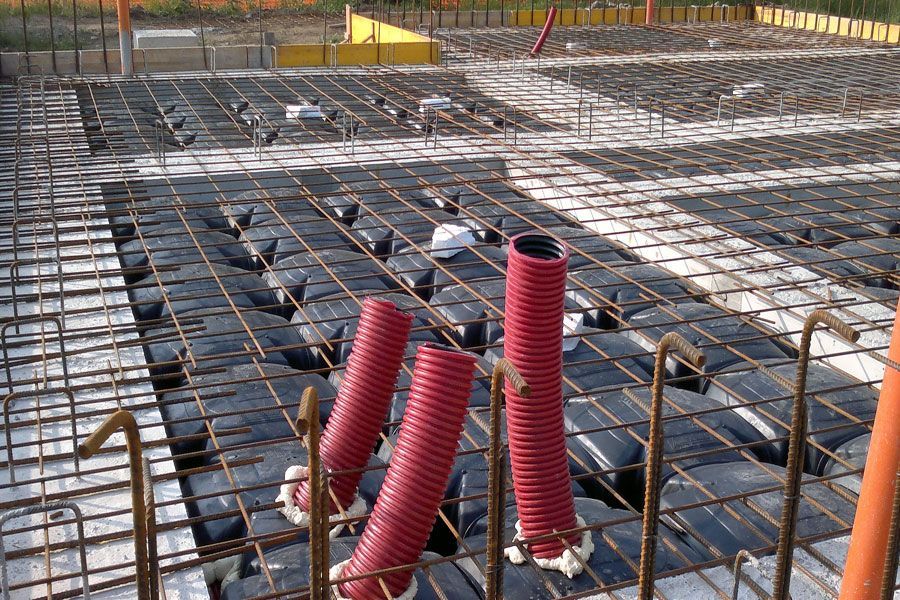 Cantiere edile con griglia di barre d'armatura e tubi corrugati rossi su una fondazione in cemento armato.