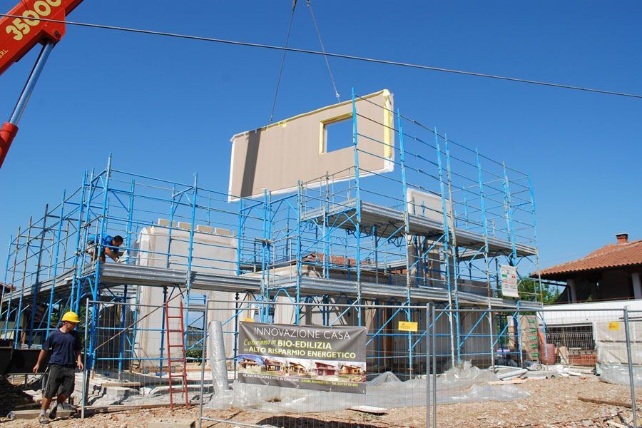 Cantiere edile con impalcature che sorreggono la struttura di una casa e operai sotto un cielo azzurro e limpido.