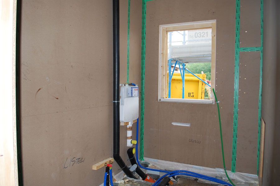 Parete interna parzialmente rifinita con cartongesso, cavi elettrici a vista e una piccola finestra che si affaccia su un edificio giallo.