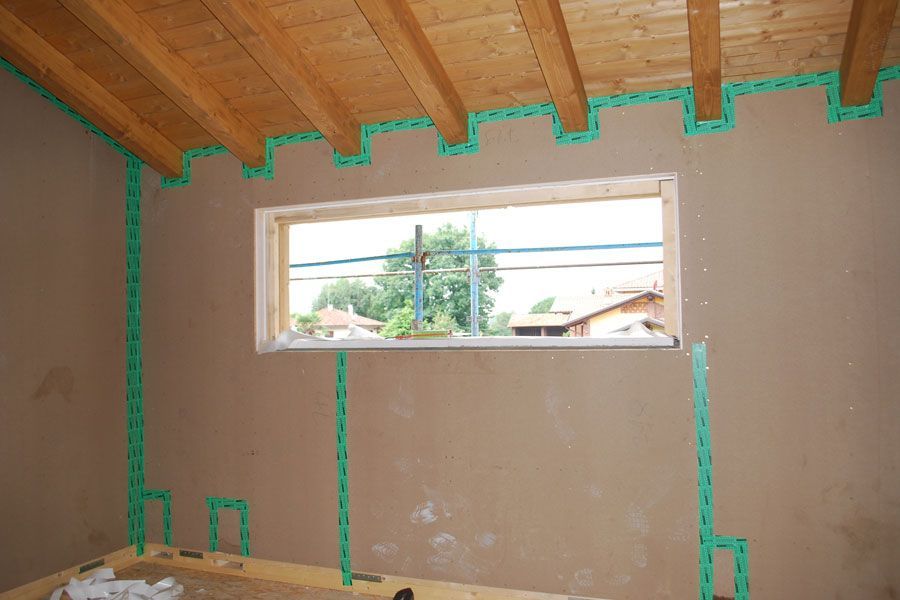 Camera parzialmente ristrutturata con travi a vista sul soffitto e finestra con vista su alberi e linee elettriche.