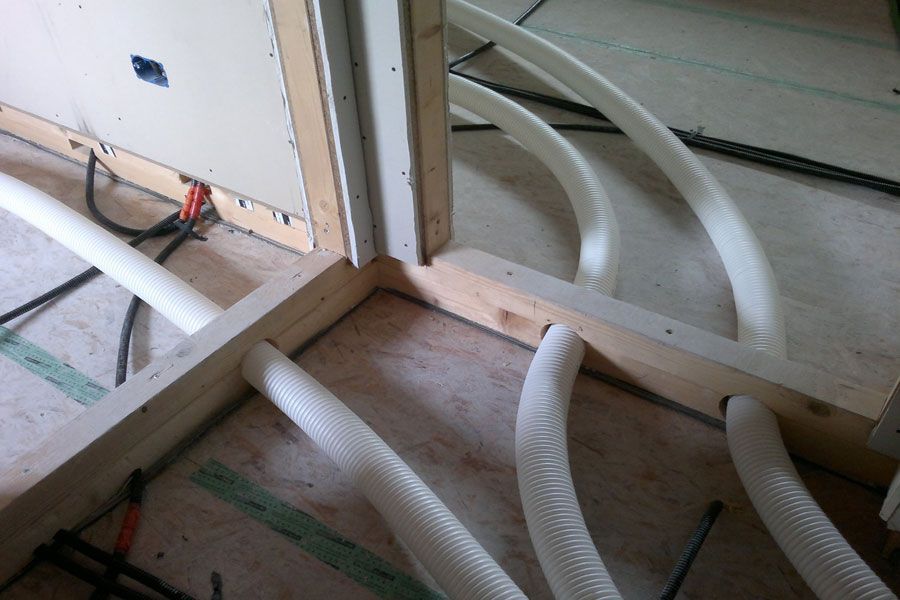 Condotti e tubi flessibili bianchi arrotolati, posati su un pavimento di legno in una stanza non rifinita.