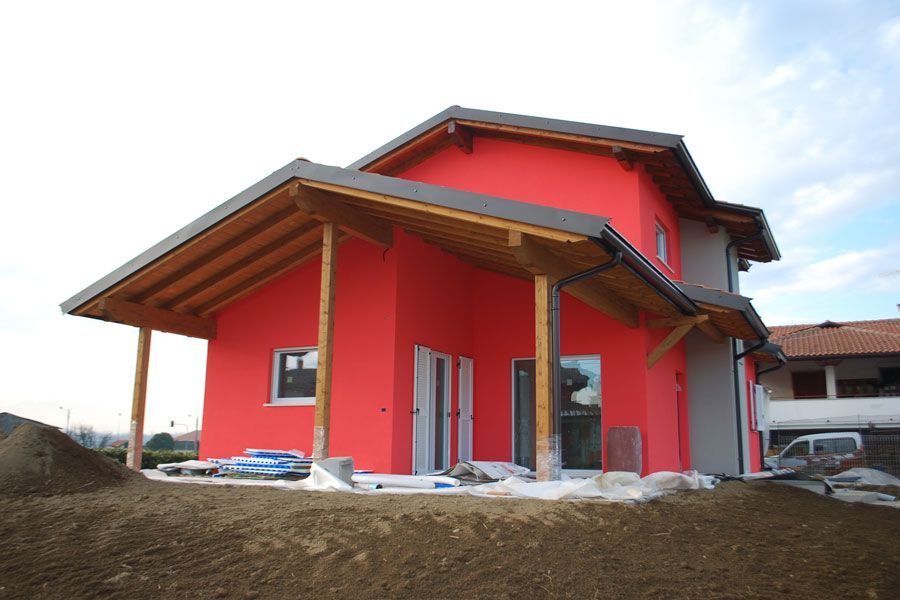 Casa rossa in costruzione con portico in legno e terra in primo piano