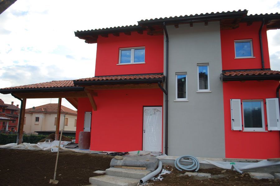 Casa a due piani rossa e grigia in costruzione, con cortile non rifinito e tubature a vista.