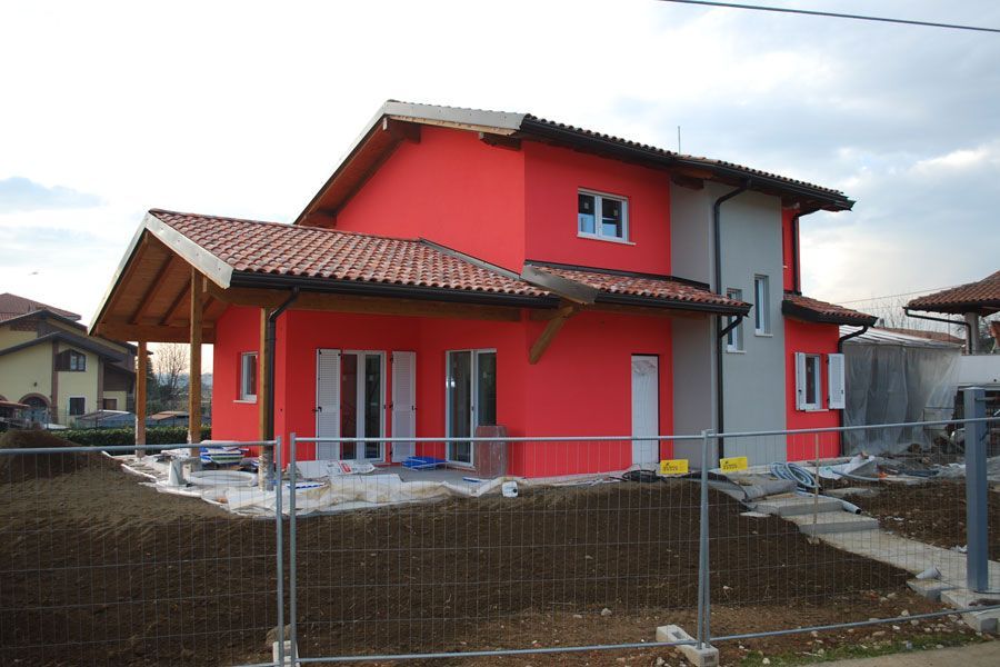 Casa rossa a due piani con tetto di tegole dietro una recinzione di filo spinato in una zona di cantiere.