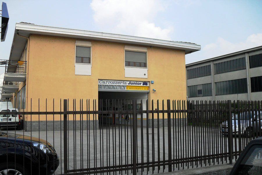 Edificio giallo a due piani dietro una recinzione metallica nera in un parcheggio.