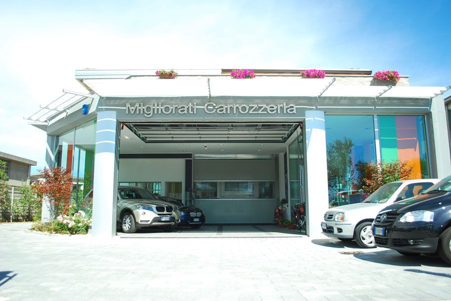 Esterno luminoso della concessionaria auto con vetture parcheggiate davanti e ingresso del garage in vetro.
