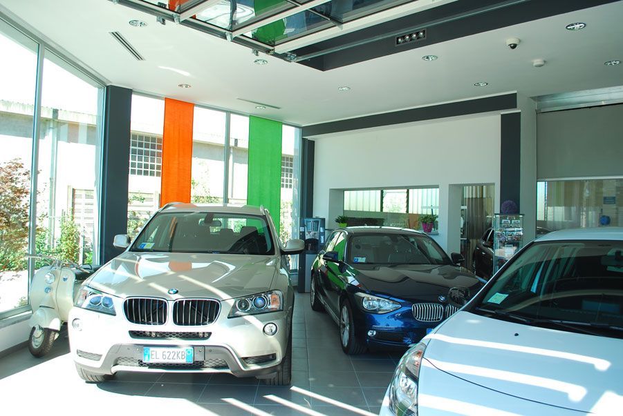 Autosalone con diverse auto parcheggiate, tra cui un SUV argentato davanti e un'auto blu sulla destra.