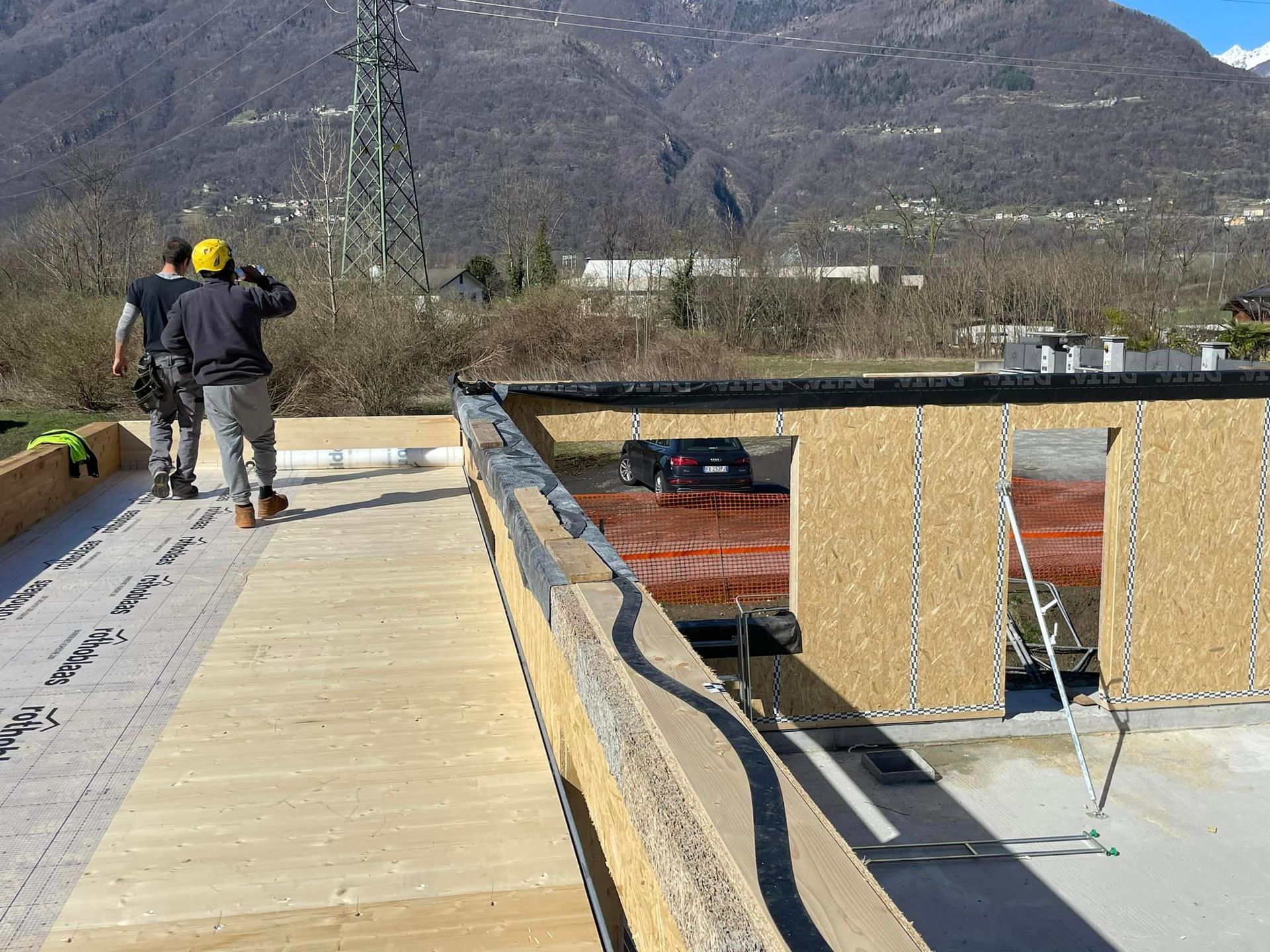 Un operaio su un tetto in costruzione con le montagne sullo sfondo.