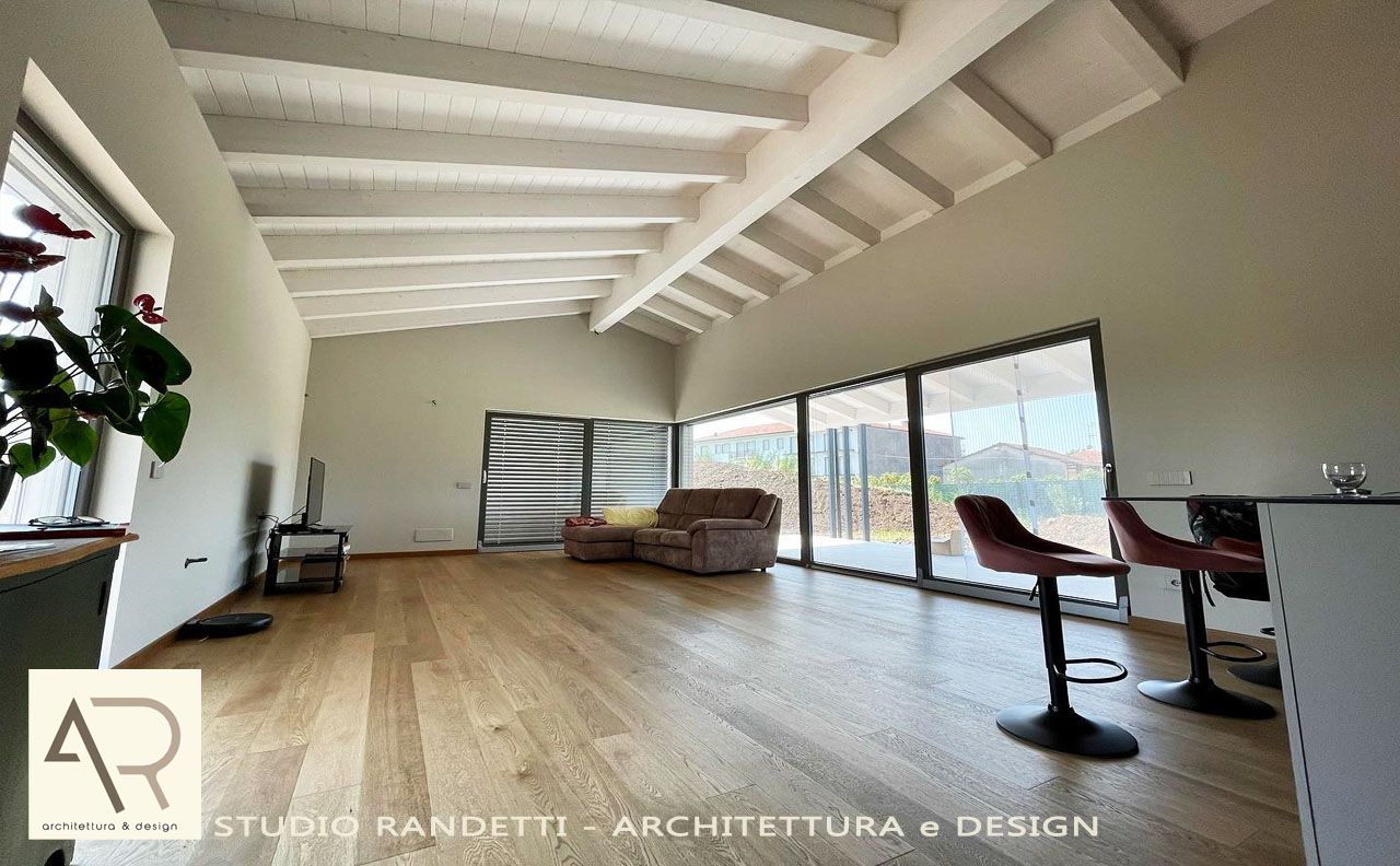 Soggiorno luminoso e arioso con pavimenti in legno, travi a vista, ampie porte scorrevoli in vetro e mobili moderni.