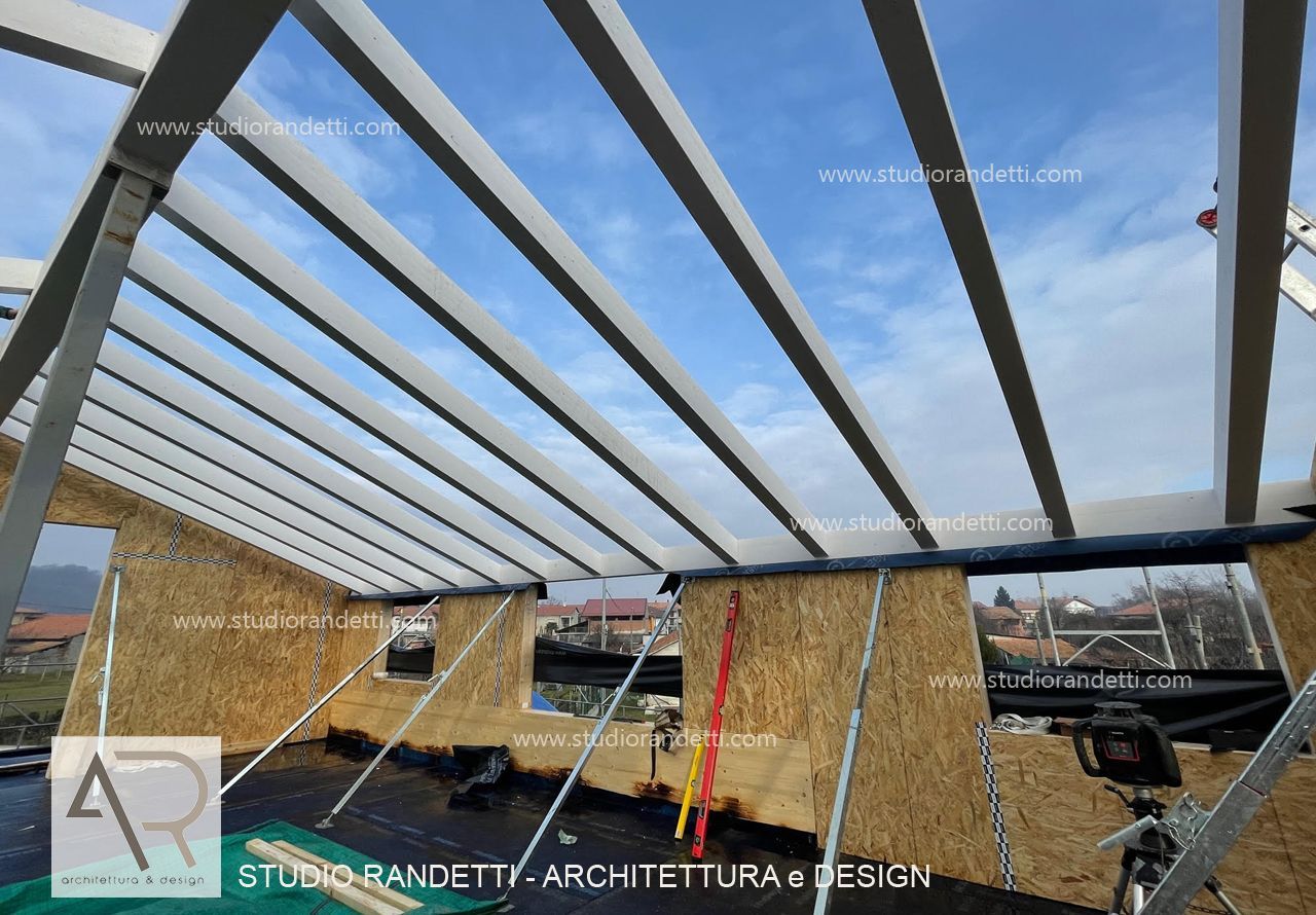 Travi d'acciaio sul tetto di una casa incompiuta in balle di paglia in un cantiere, con il cielo aperto sopra.