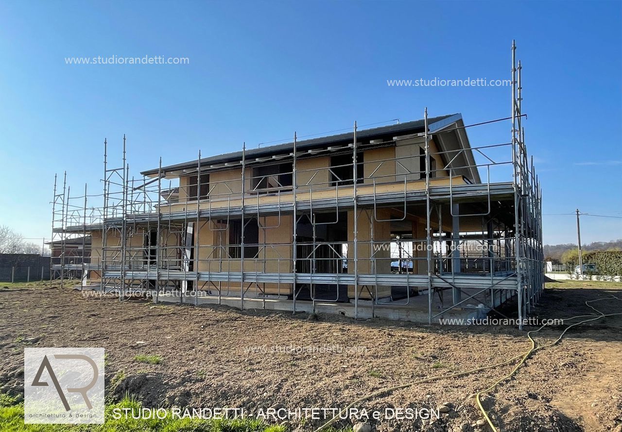 Casa a due piani in costruzione con impalcature in un campo rurale sotto un cielo azzurro