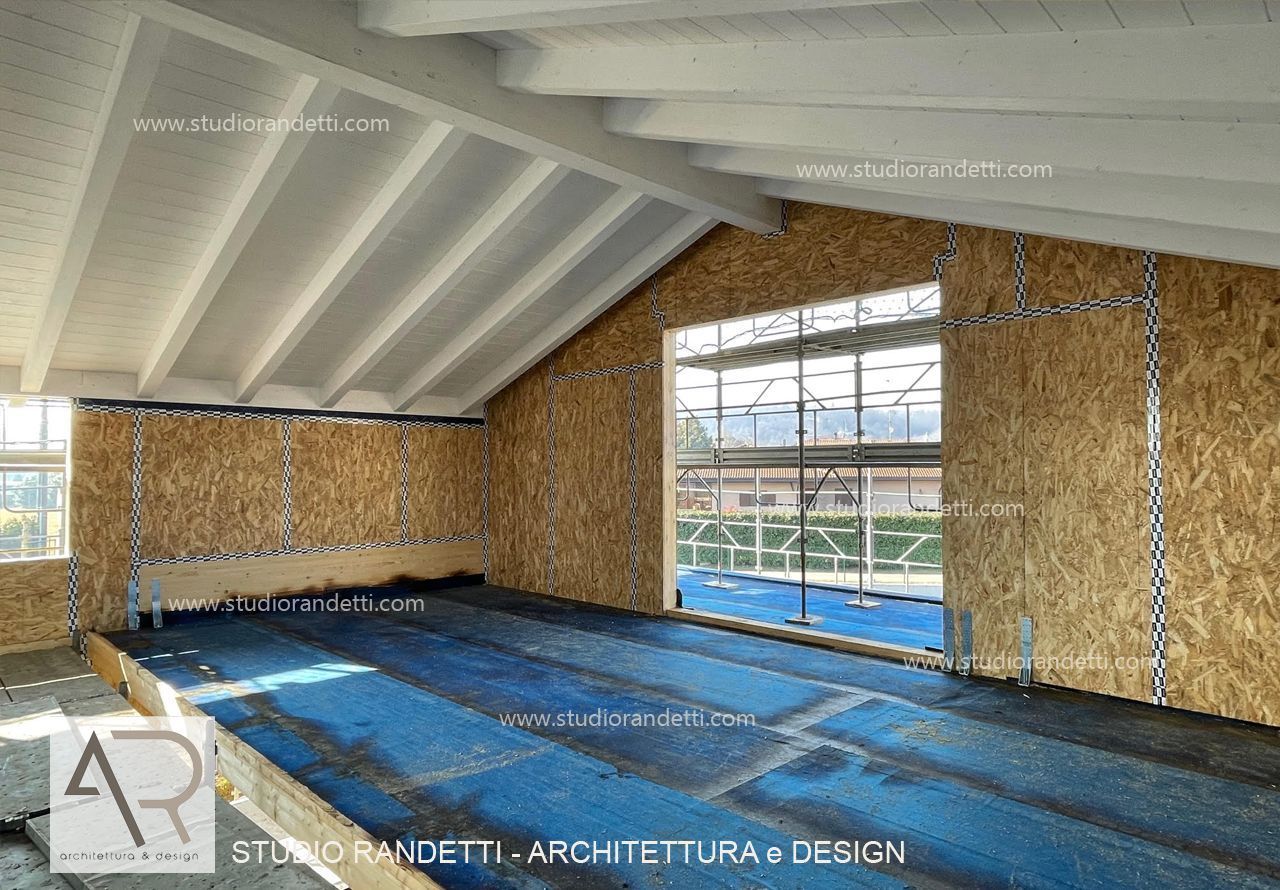 Interno di una stanza con pavimento blu, soffitto bianco inclinato, pareti in legno e grandi finestre in fase di costruzione.