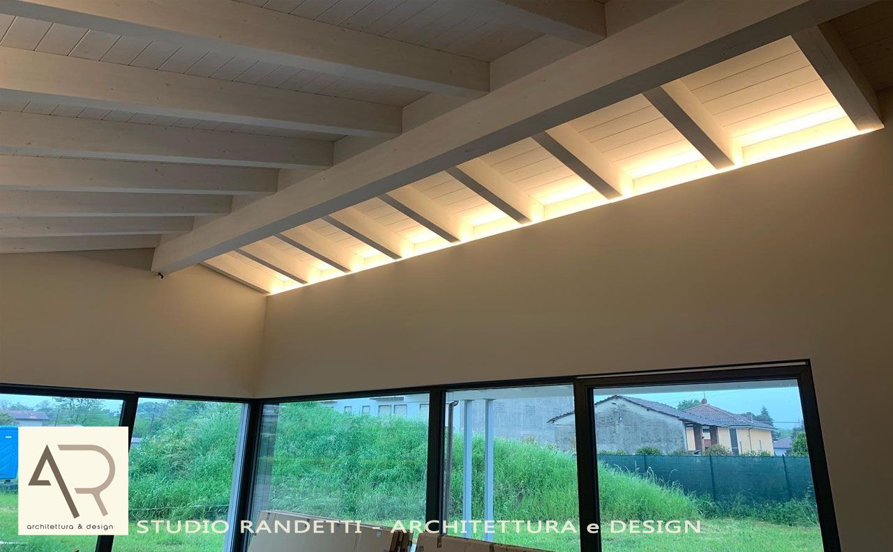 Interni con soffitto inclinato bianco, travi a vista e ampie finestre che si affacciano su un paesaggio verdeggiante.