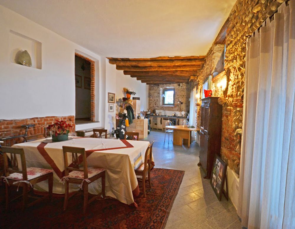 Sala da pranzo rustica con tavolo apparecchiato, pareti in pietra a vista, travi in legno e illuminazione calda.