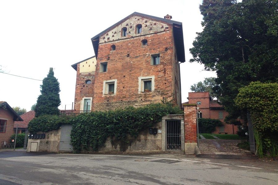 Casa in mattoni con muro e cancello ricoperti di edera, in una strada tranquilla sotto un cielo nuvoloso.