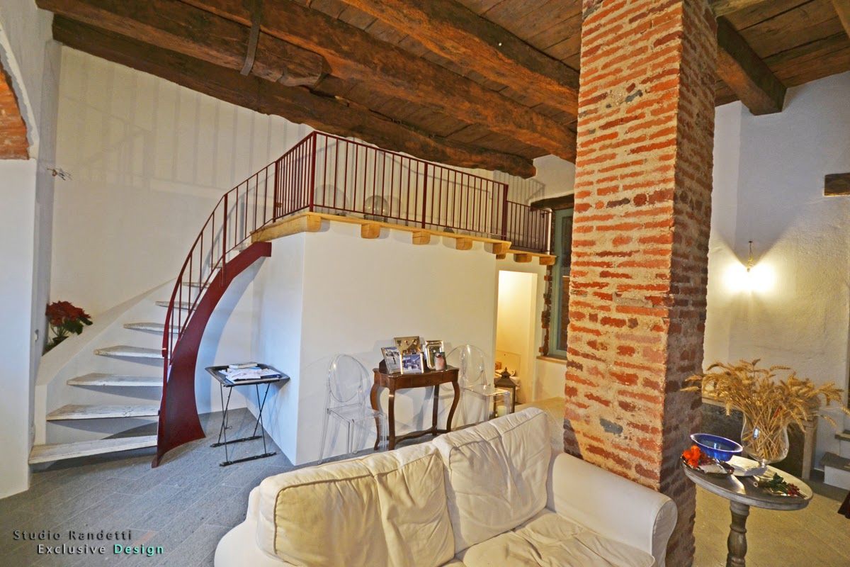 Accogliente soggiorno con scala a chiocciola, colonna in mattoni a vista, travi in ​​legno e divano bianco.