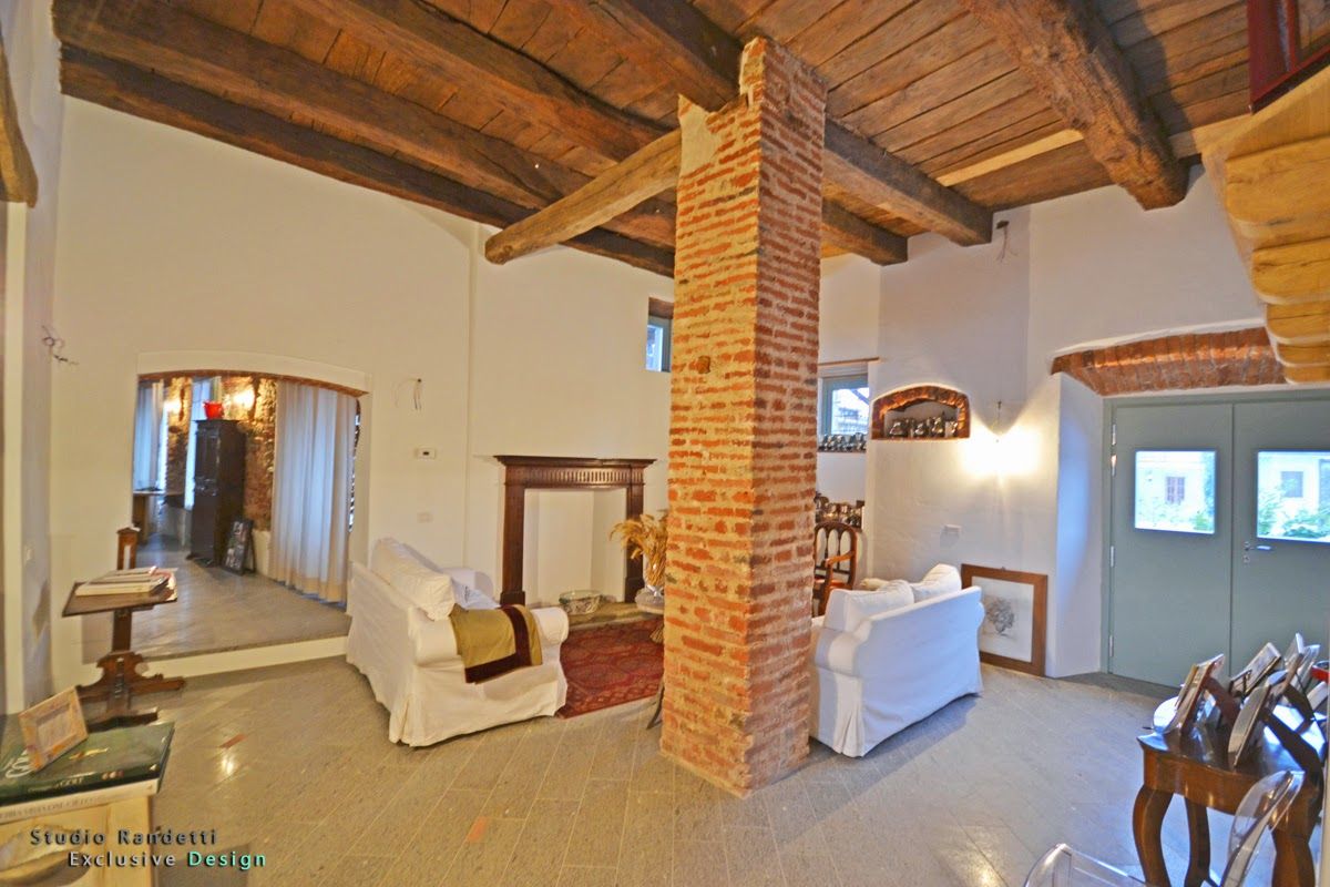 Soggiorno rustico con travi a vista, colonna in mattoni, divani bianchi e illuminazione calda.