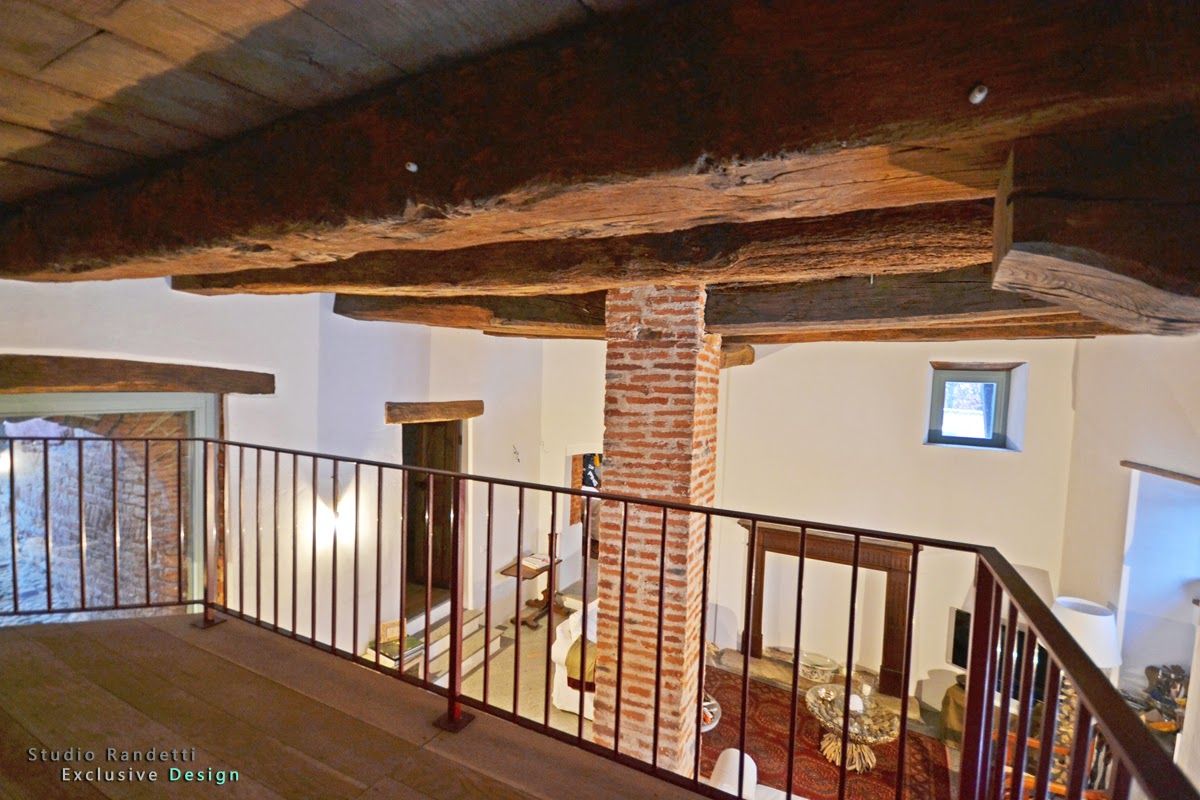 Interno di un loft con travi a vista, camino in mattoni e ringhiera in metallo che si affaccia su un piano inferiore.