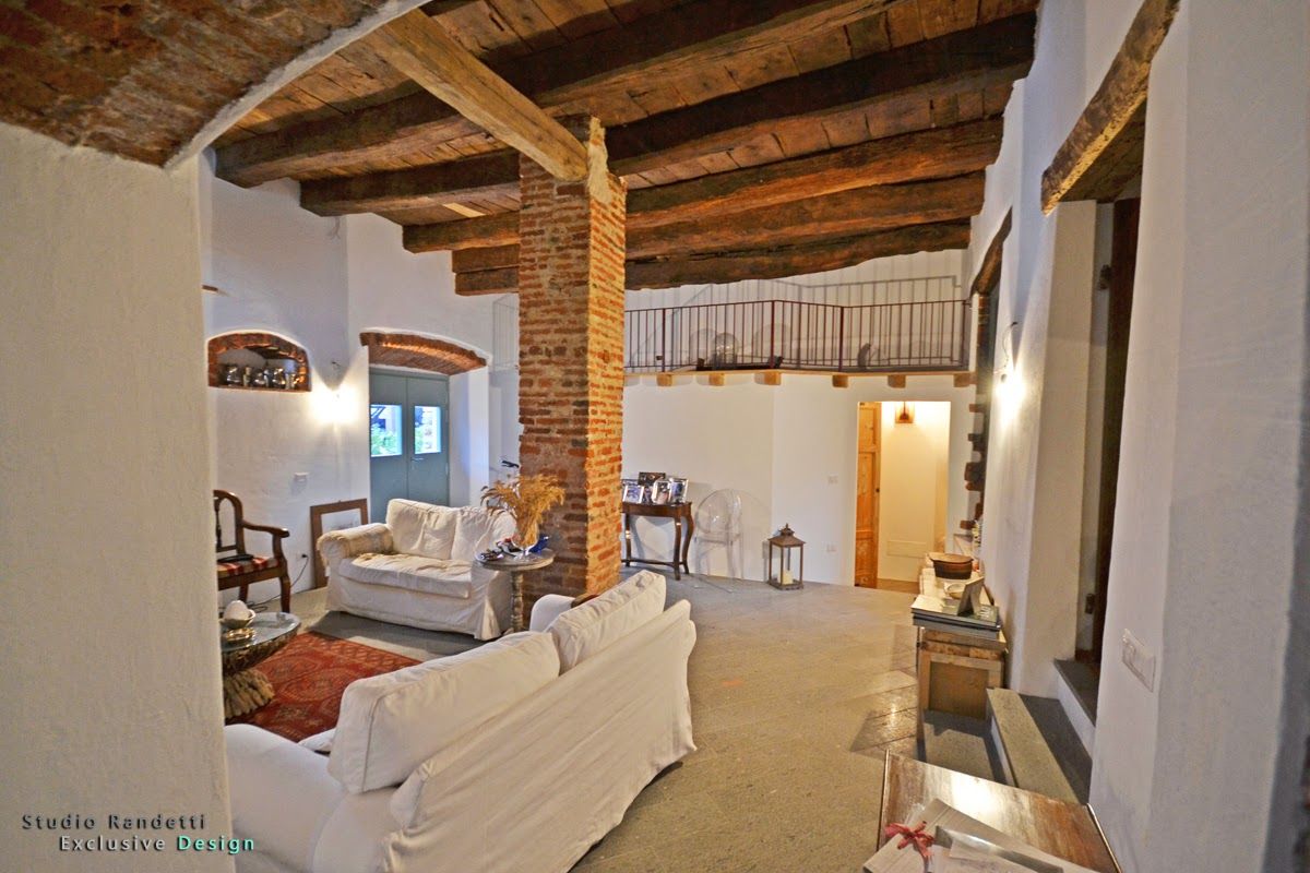 Soggiorno rustico con travi in ​​legno a vista, camino in pietra, divani bianchi e soffitto alto.