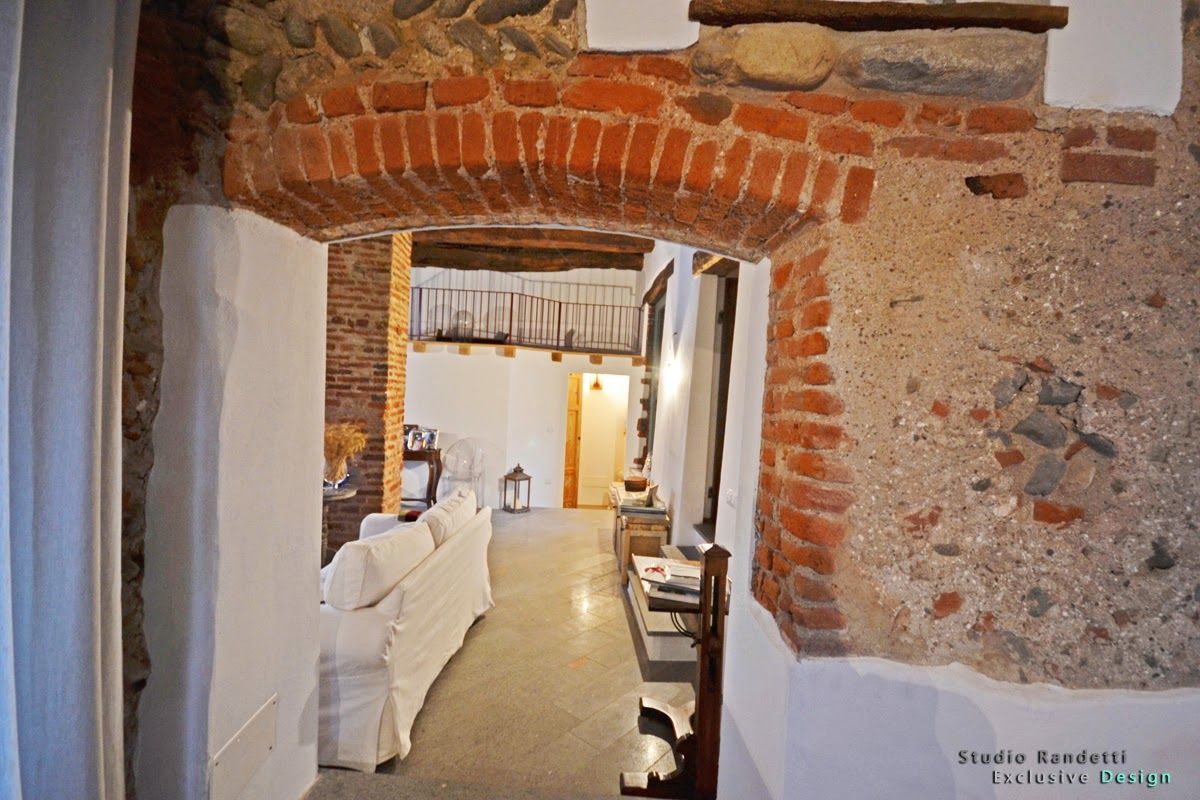 Interno rustico con un arco in mattoni, mobili rivestiti di bianco e un corridoio che conduce a una stanza illuminata da una luce calda.