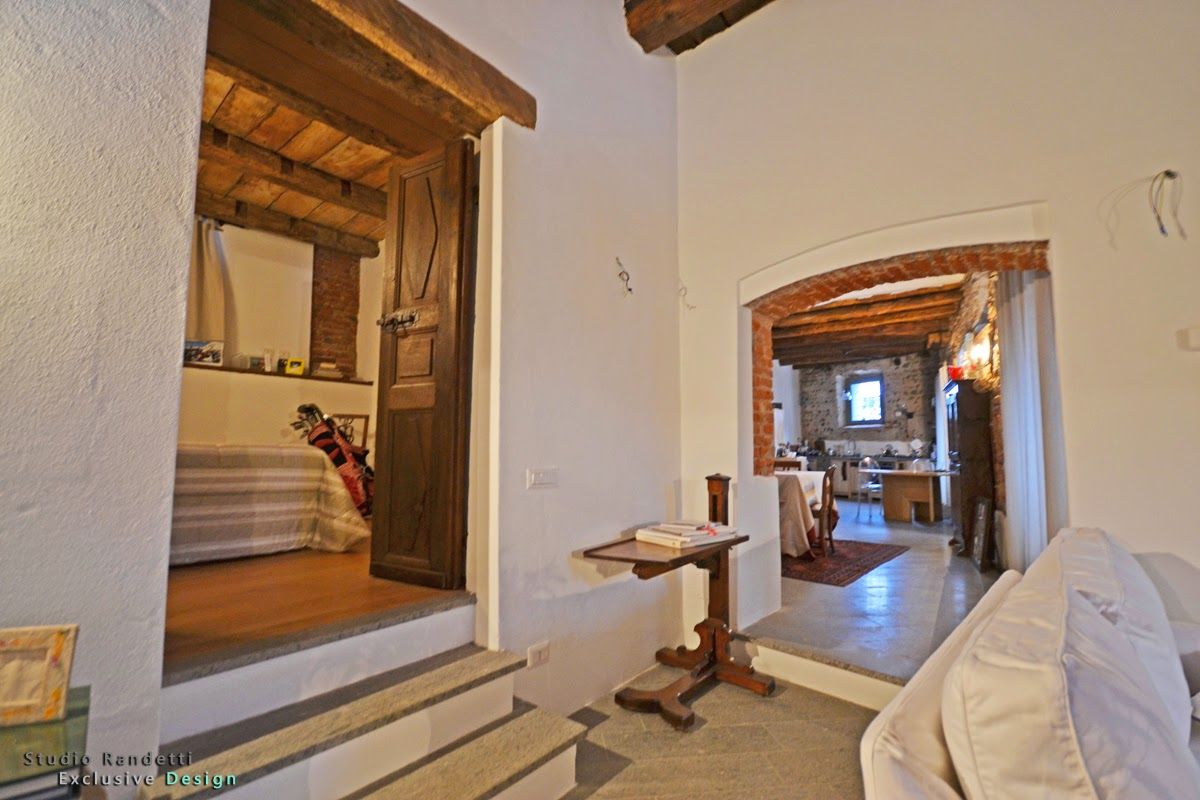 Interno rustico con travi in ​​legno, archi e una scala che conduce a un corridoio luminoso.