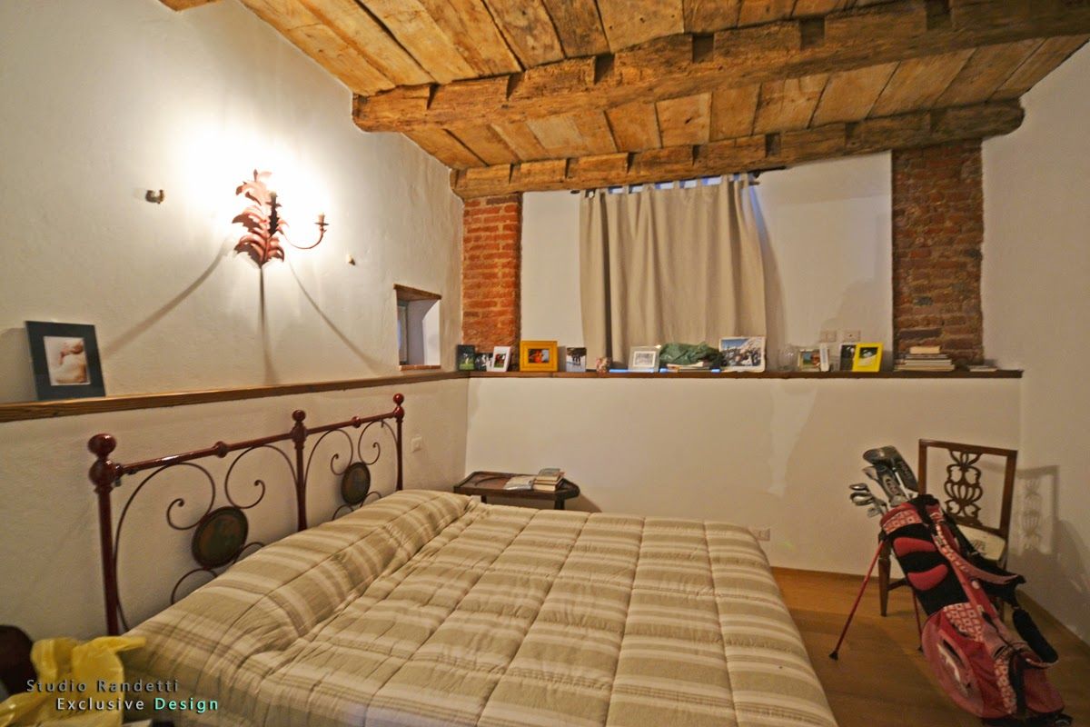 Accogliente camera da letto con letto in ferro battuto, soffitto con travi a vista, dettagli in mattoni e una finestra con tende.