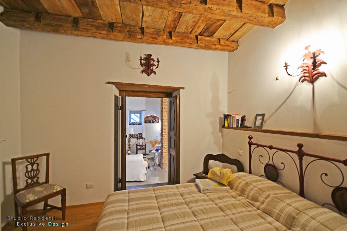 Camera da letto rustica con soffitto in legno, letto in ferro battuto e porta che conduce a una luminosa stanza adiacente.
