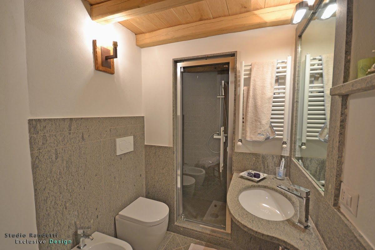 Piccolo bagno con pareti in pietra, doccia in vetro, WC bianco e lavabo sotto un soffitto inclinato in legno.