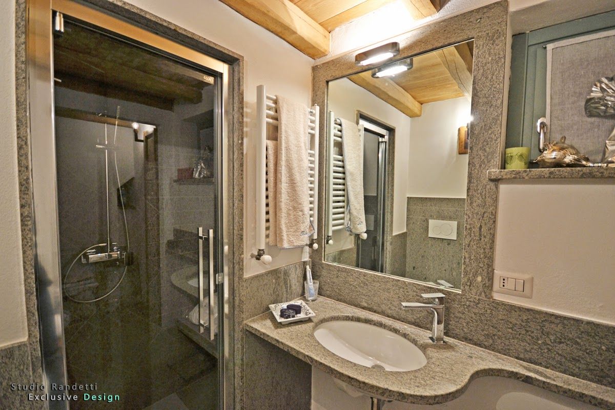 Bagno con mobile lavabo in granito, ampio specchio e box doccia in vetro sotto travi in ​​legno a vista.