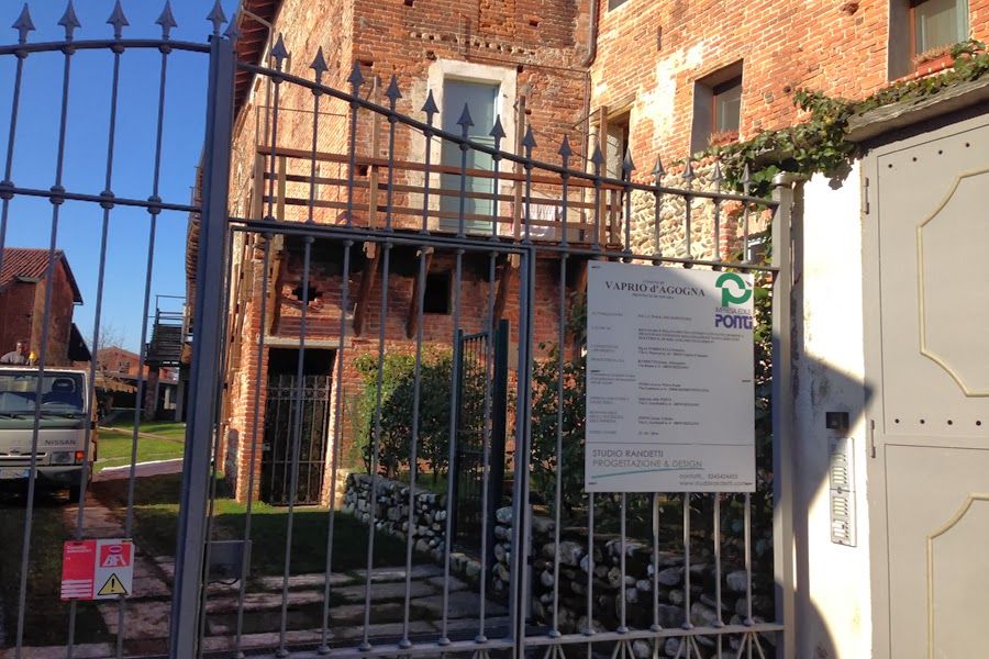 Ingresso di un edificio in mattoni con cancello e cartello, visto dalla strada sotto un cielo azzurro.