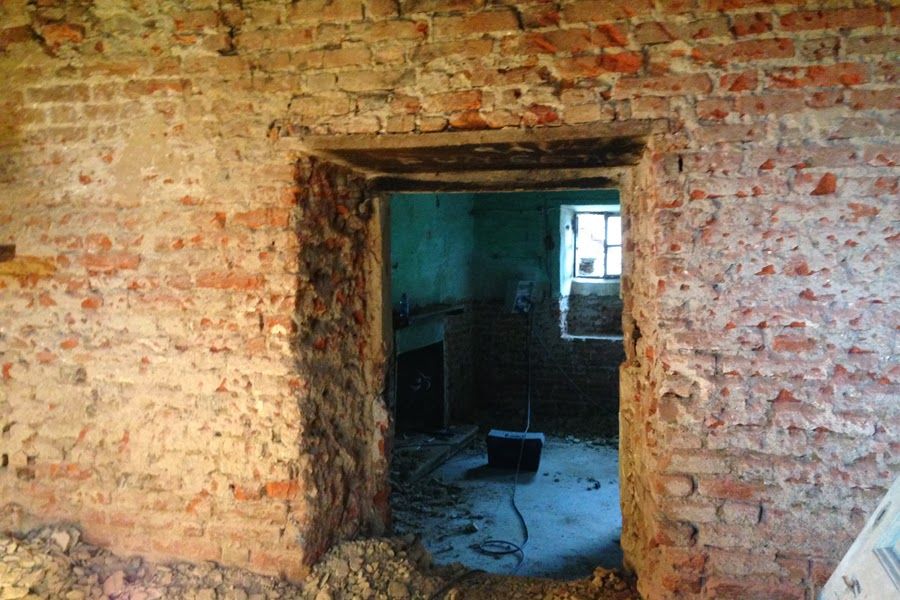 Vecchio muro di mattoni con una porta che si apre su una stanza buia e abbandonata con una sedia e una finestra.