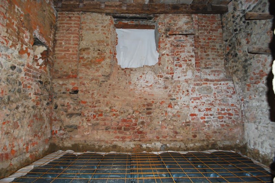 Interno in mattoni a vista con una piccola finestra con tenda e pavimento a griglia blu in costruzione